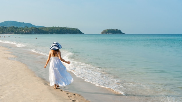 Szczęśliwa Podróżniczka Azjatycka Kobieta W Biel Sukni Cieszy Się Na Tropikalnej Plaży Na Wakacje. Koncepcja Lato Na Plaży.