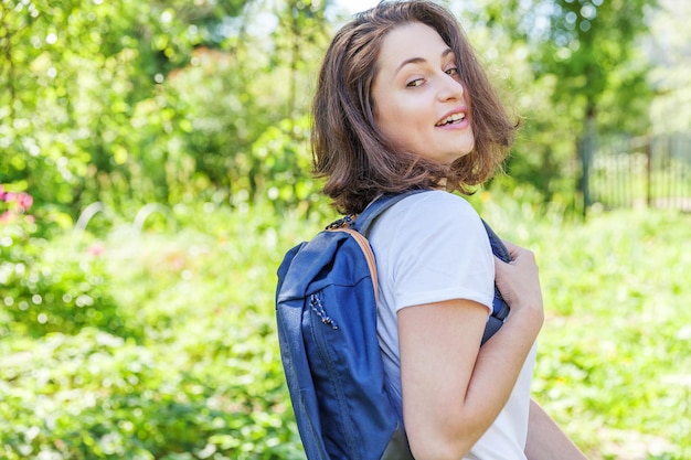 Szczęśliwa pozytywna studentka z plecakiem uśmiechnięta na zielonym tle parku kobieta odpoczywa na obozie...