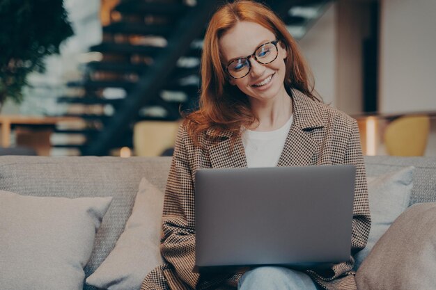 Szczęśliwa pracownica biurowa rozmawiająca na laptopie siedząc na szarej kanapie w biurze