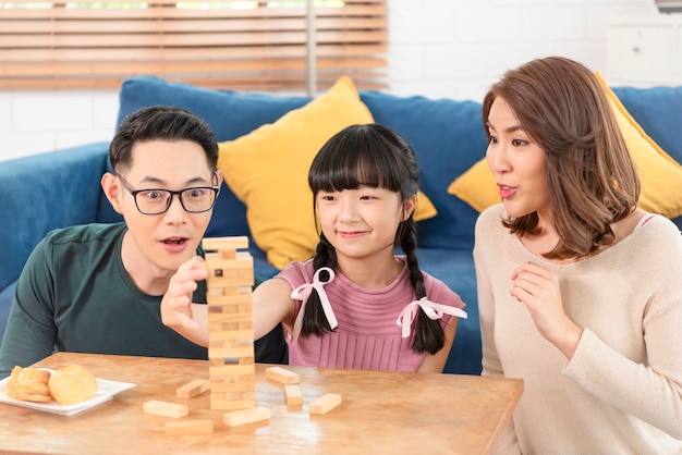 Szczęśliwa rodzina azjatycka bawi się grając w grę blokową w salonie w domu.