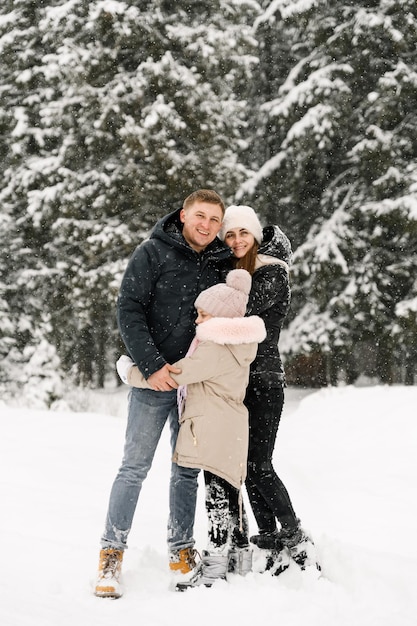 Szczęśliwa rodzina bawi się w zimowym lesie. Matka, ojciec i córka bawią się śniegiem. Koncepcja rodziny