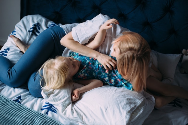 Szczęśliwa rodzina blond mama i córka bawią się i bawią w łóżku.