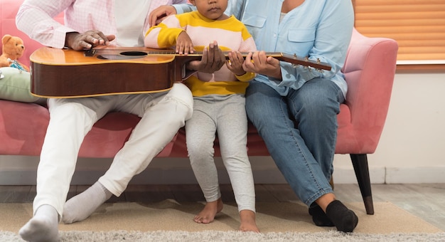 Szczęśliwa rodzina grająca razem na gitarze na kanapie w salonie w domu