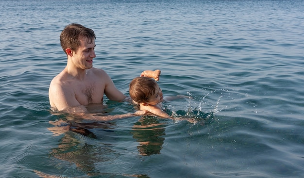 Szczęśliwa rodzina i zdrowy styl życia. Młody ojciec uczy dziecko pływać w morzu