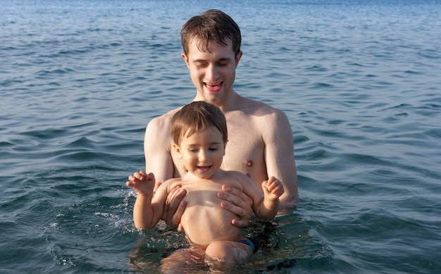 Szczęśliwa rodzina i zdrowy styl życia. Młody ojciec uczy dziecko pływać w morzu