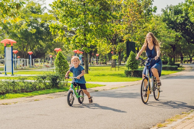 Szczęśliwa rodzina jeździ na rowerach na świeżym powietrzu i uśmiecha się. Mama na rowerze i syn na balancebike