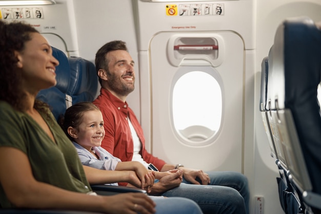 Szczęśliwa rodzina kaukaska, rodzice z córeczką uśmiechnięci i trzymający się za ręce podczas siedzenia w samolocie. Transport, koncepcja wakacji