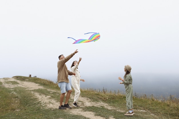 Szczęśliwa rodzina koncepcja. rodzice i dziecko bawią się kolorowym latawcem. Młoda matka, ojciec i córeczka, zabawy razem na świeżym powietrzu w mglisty dzień.