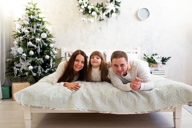 Szczęśliwa rodzina leżąc w łóżku w pobliżu choinki w domu