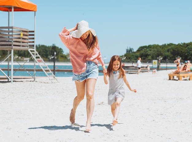 Szczęśliwa rodzina mama i córka biegają śmiać się i bawić na plaży mama i dwie dziewczyny na plaży