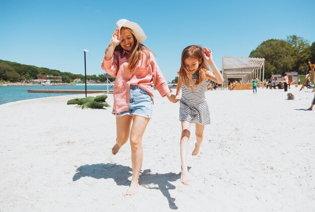 Szczęśliwa rodzina mama i córka biegają śmiać się i bawić na plaży mama i dwie dziewczyny na plaży