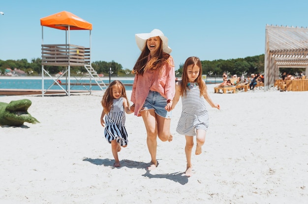 Szczęśliwa rodzina mama i córka biegają śmiać się i bawić na plaży mama i dwie dziewczyny na plaży