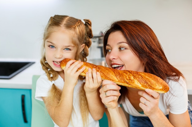 Szczęśliwa rodzina, mama i córka jedzą jeden chleb gryzący z różnych stron. Relacje rodzinne dziecka z rodzicami