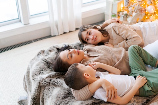 Szczęśliwa rodzina mama i dwoje dzieci leżących na łóżku czekających na Boże Narodzenie i śmiejąc się