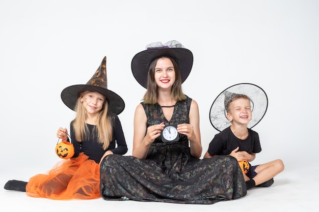 Szczęśliwa rodzina matka i dzieci w przerażających strojach wiedźmy i czarnoksiężnika, trzymające czarne zegarki i kosze z smakołykami