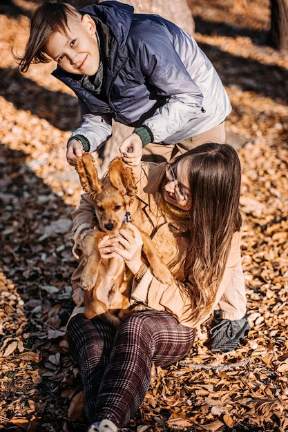 Szczęśliwa rodzina matka i nastoletni syn bawią się ze szczeniakiem cocker spaniela w jesiennym parku