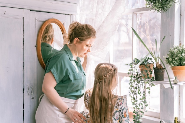 Szczęśliwa rodzina matka z małą córką córką bawi się na przedmieściach wsi życie domowe w słoneczny wiosenny dzień szczera mama i dzieci stoją przy oknie z roślinami, którzy kochają i troszczą się o chwilę