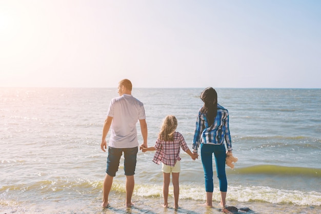 Szczęśliwa rodzina na plaży. Ludzie bawią się na wakacjach. Ojcuje, matka i dziecko przeciw błękitnemu tłu morza i nieba. Koncepcja podróży wakacyjnych