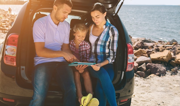 Szczęśliwa rodzina na wycieczce samochodowej w samochodzie. Tata, mama i córka podróżują nad morzem, oceanem lub rzeką. Letnia jazda samochodem