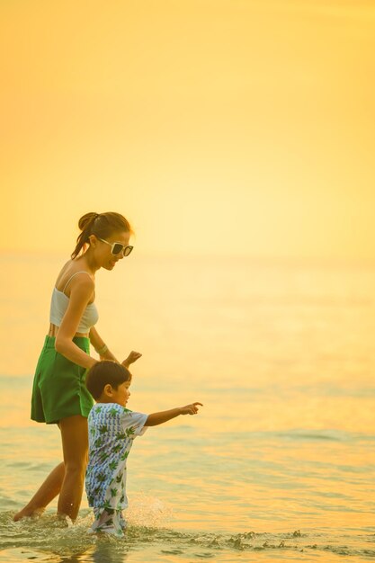 Szczęśliwa rodzina odpoczynku na plaży w lecie Matka i baby boy stóp na pianie morskiej na światło słoneczne woda się porusza