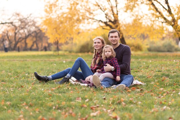 Szczęśliwa rodzina odpoczywa w lesie jesienią. Mama, tata i córka siedzą w jesiennym parku.