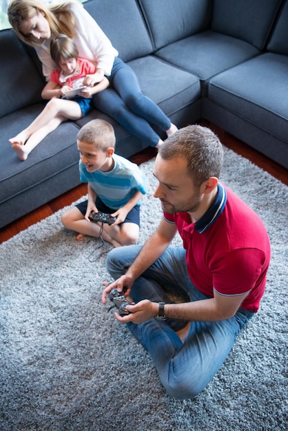 Szczęśliwa rodzina. Ojciec, matka i dzieci grają w grę wideo Ojciec i syn grają razem w gry wideo na podłodze