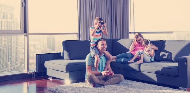 Szczęśliwa rodzina. Ojciec, matka i dzieci grają w grę wideo Ojciec i syn grają razem w gry wideo na podłodze