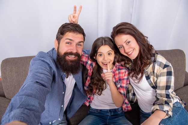 Szczęśliwa rodzina robi selfie siedząc na kanapie w domu