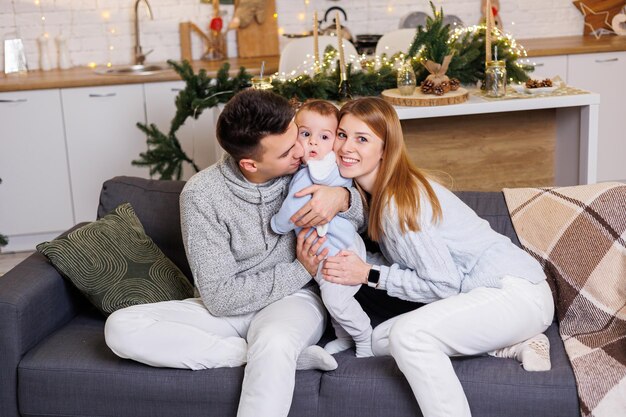 Zdjęcie szczęśliwa rodzina siedzi na kanapie z małym synkiem przy choince i uśmiecha się radośnie domowa świąteczna atmosfera nowego roku