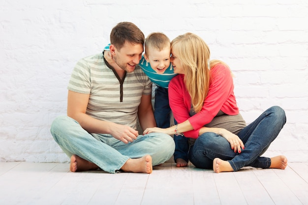 Szczęśliwa rodzina składająca się z trzech osób siedzi na podłodze i się śmieje