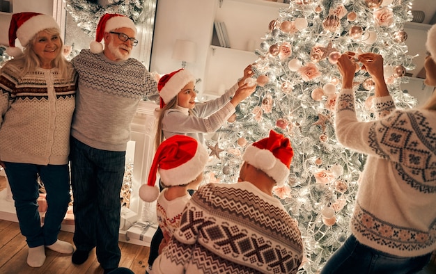 Zdjęcie szczęśliwa rodzina w czerwonym kapeluszu dekoruje choinkę