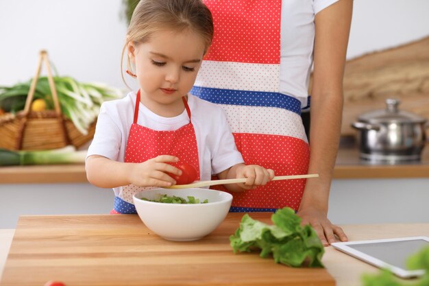 Szczęśliwa rodzina w kuchni Córka mama i dziecko gotują smaczne śniadanie ze świeżej sałatki Mały pomocnik kroi i miesza pomidory z zielenią