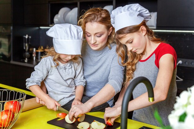 Zdjęcie szczęśliwa rodzina w kuchni. matka i dwoje dzieci przygotowują ciasto, upiec szarlotkę. mama i córki, gotowanie zdrowej żywności w domu i zabawę. gospodarstwo domowe, pomoc w pracy zespołowej, koncepcja macierzyństwa