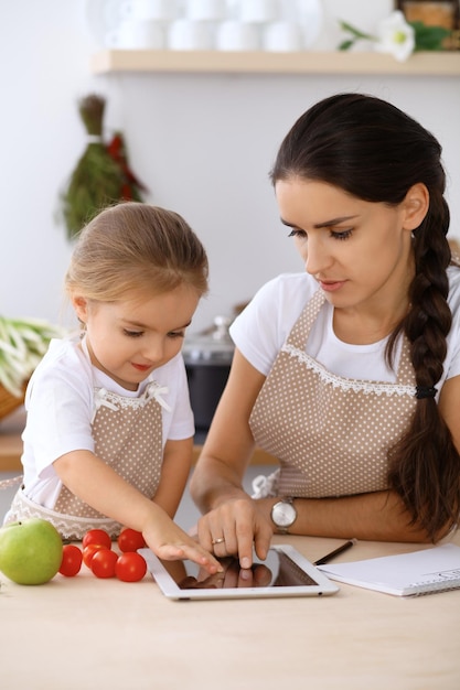 Zdjęcie szczęśliwa rodzina w kuchni matka z córką przygotowują menu do gotowania smacznego śniadania w kuchni mały pomocnik jest gotowy do pracy w gospodarstwie domowym