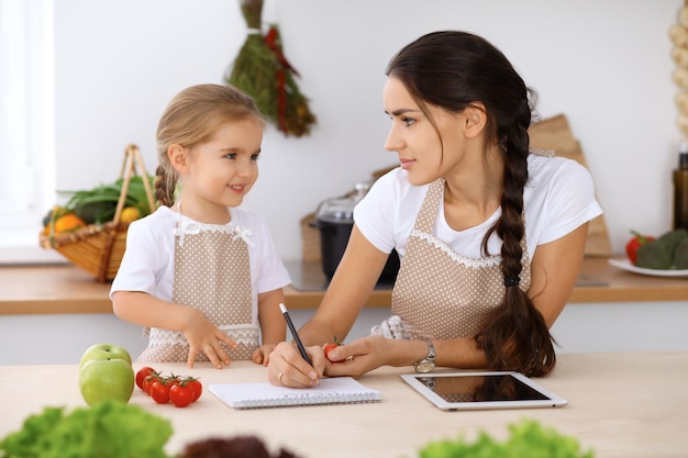 Szczęśliwa rodzina w kuchni Matka z córką przygotowują menu do gotowania smacznego śniadania w kuchni Mały pomocnik jest gotowy do pracy w gospodarstwie domowym