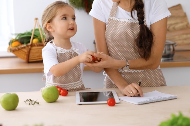 Szczęśliwa rodzina w kuchni Matka z córką przygotowują menu do gotowania smacznego śniadania w kuchni Mały pomocnik jest gotowy do pracy w gospodarstwie domowym