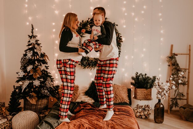 Szczęśliwa rodzina w piżamie z rodzicami bawić się z dzieckiem skaczącym na łóżku w sypialni. noworoczne ubrania rodzinne wyglądają stroje. Prezenty na Walentynki