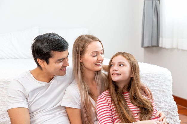 Szczęśliwa rodzina, w tym matka ojca i córka, siedzą przed łóżkiem z uśmiechem patrząc na siebie