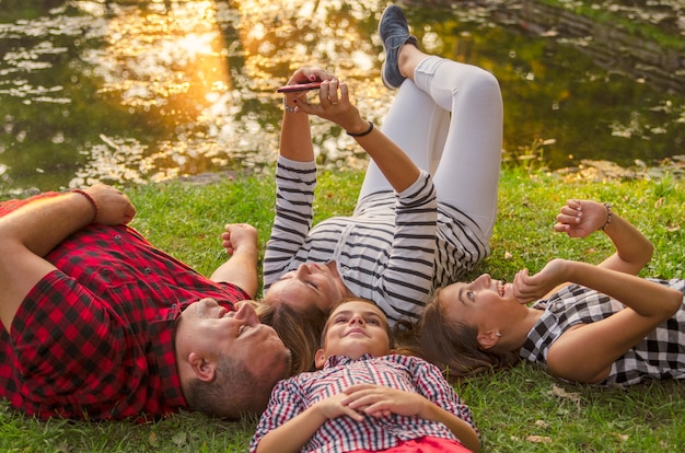 Szczęśliwa rodzina wpólnie kłaść na zielonej trawie i bierze selfie z telefonem komórkowym