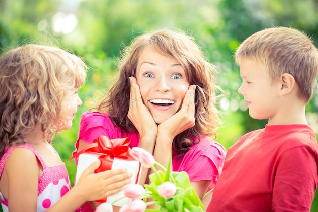 Szczęśliwa rodzina z bukietem kwiatów i prezentów na zewnątrz Młoda piękna matka z synem i córką leżącą na zielonej trawie Koncepcja wakacji wiosennych Dzień matki Niespodzianka i radość