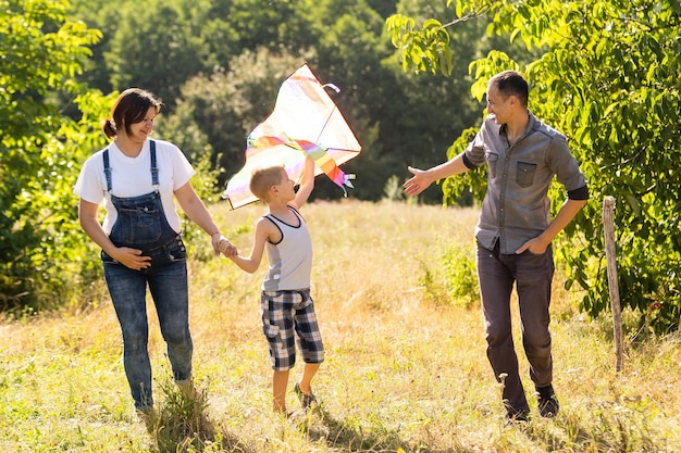 Szczęśliwa rodzina z ciężarną żoną latają razem latawcem w letnim polu