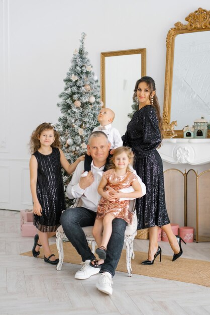 Szczęśliwa rodzina z uroczymi dziećmi noszą razem choinkę w domu świętując Boże Narodzenie i nowy rok