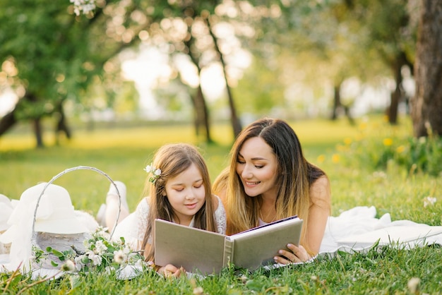 Szczęśliwa rodzinna mama i córka oglądają album ze zdjęciami latem w parku lub w ogrodzie