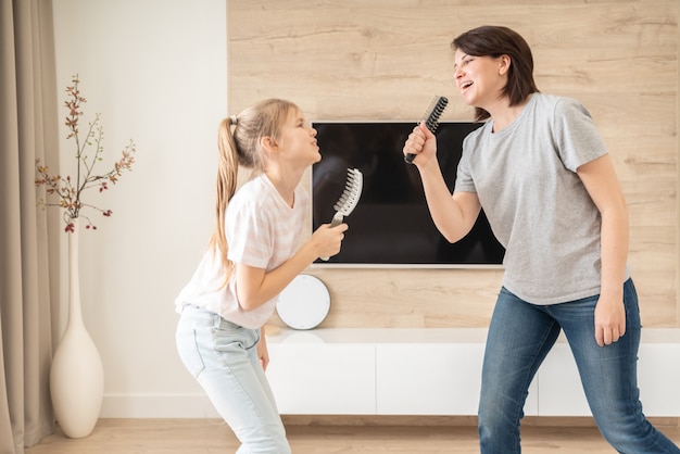 Szczęśliwa rodzinna młoda dorosła matka i śliczna nastoletnia córka ma zabawę śpiewa piosenkę karaoke w szczotkach do włosów.