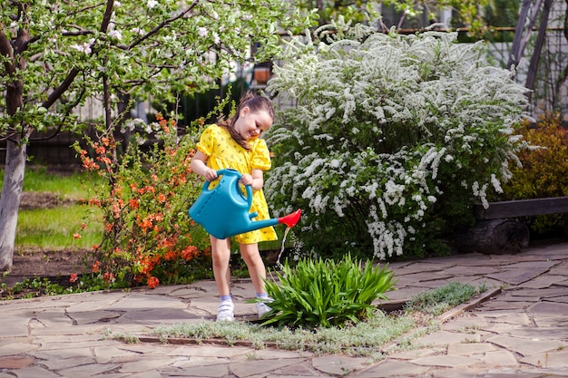 Szczęśliwa roześmiana dziewczyna w żółtej sukience podlewa kwiaty z niebieskiej konewki młodego ogrodnika...