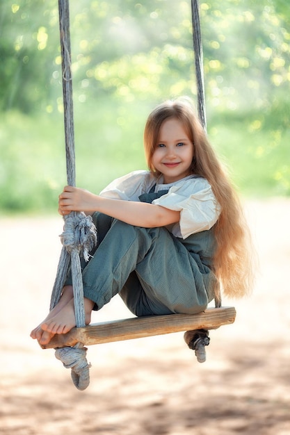 Szczęśliwa roześmiana dziewczynka z długimi włosami, ciesząca się przejażdżką huśtawką w słoneczny letni dzień