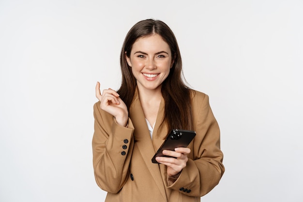 Szczęśliwa roześmiana kobieta trzymająca smartfon i uśmiechnięta bizneswoman używająca telefonu komórkowego stojącego nad w...