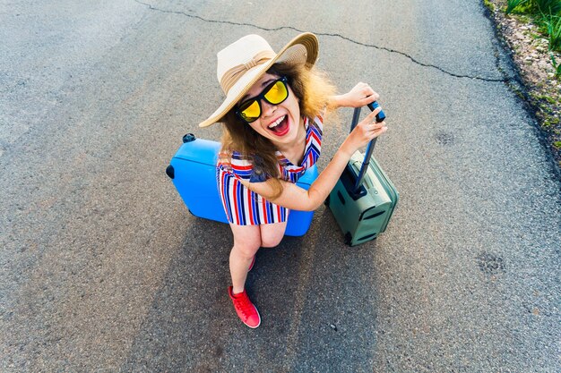 Szczęśliwa roześmiana młoda kobieta z walizkami na drodze.