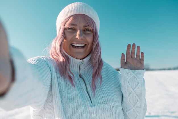 Zdjęcie szczęśliwa różowa kobieta turystka odbywająca połączenie wideo lub robiąca selfie w zimowych wakacjach w śnieżnym