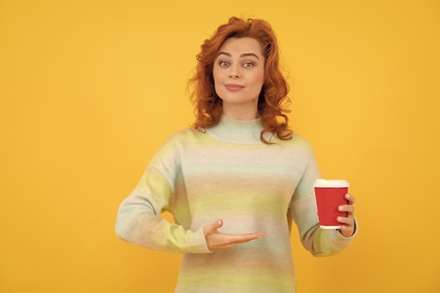 Szczęśliwa ruda kobieta prezentuje produkt kawy na wynos w filiżance picia kawy